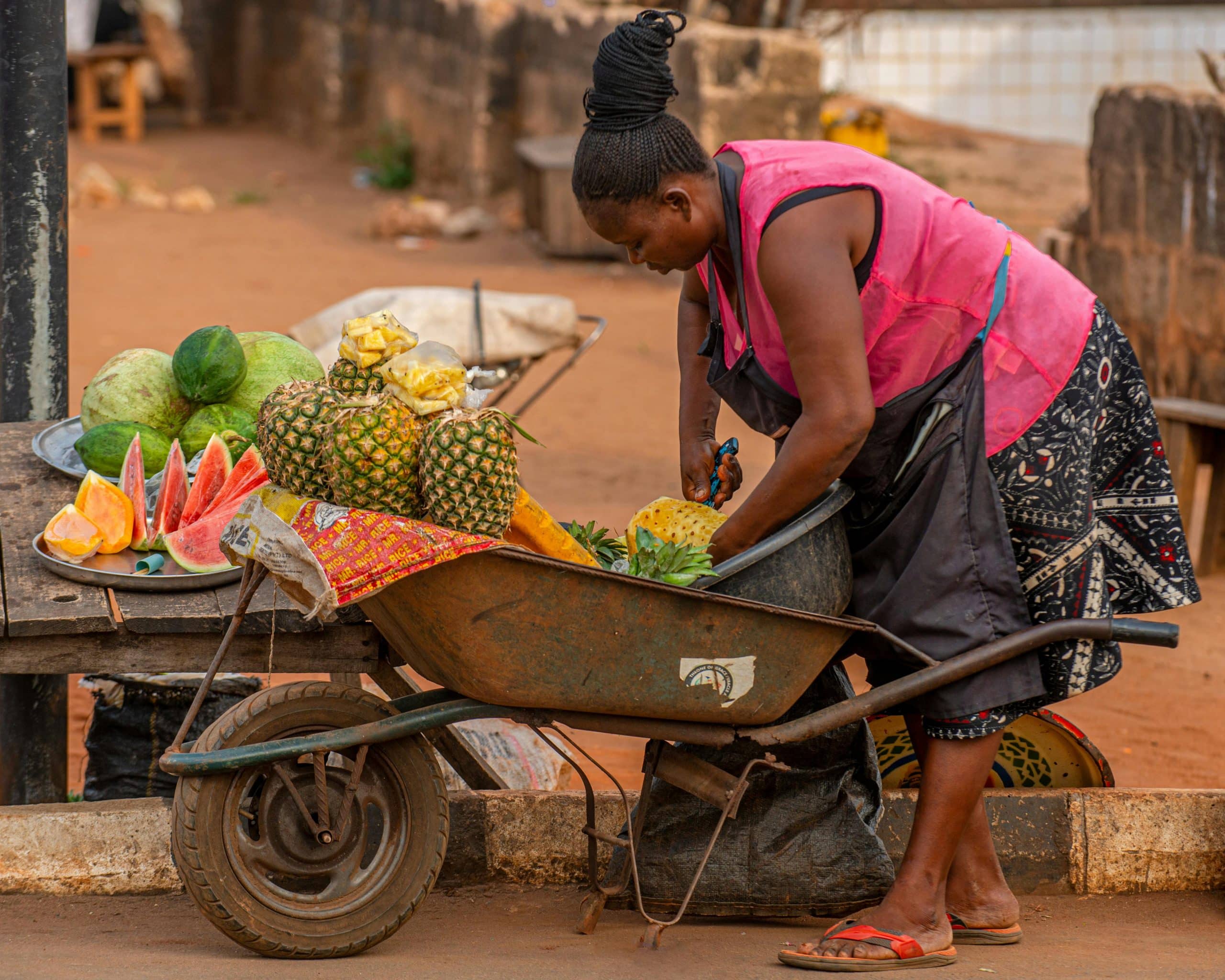 African woman preparing fresh pineapples on a street vendor wheelbarrow in a local market, a signal for gender inclusion in Malawi.