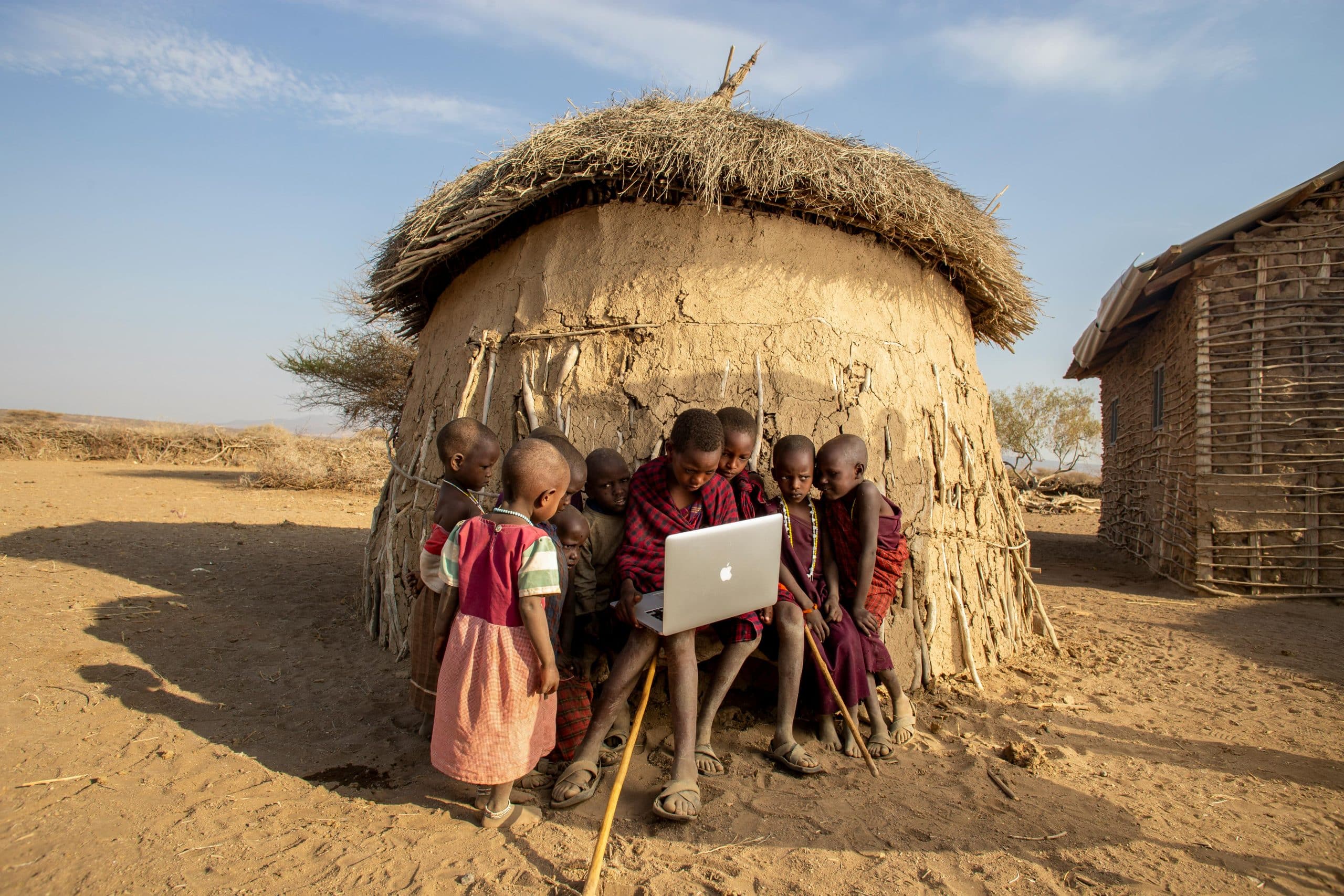 Macra Group of African children in a Tanzanian village using a laptop outdoors, engaged in learning.
